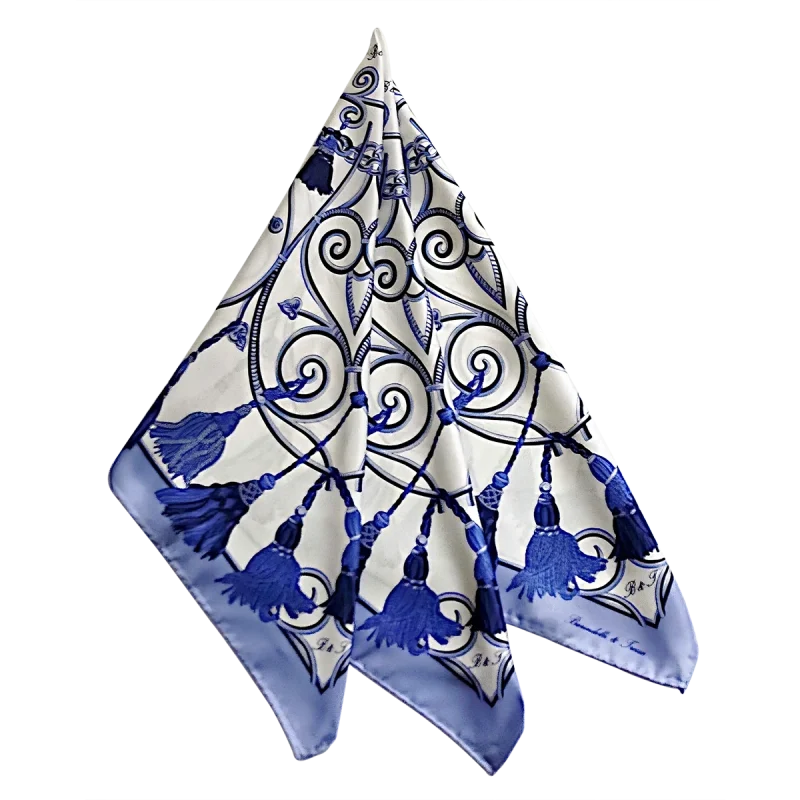 foulard in seta drappeggiato con corde e nappine blu su fondo chiaro