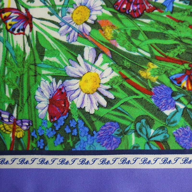 dettaglio di foulard in seta con margherite, farfalle, vegetazione verde e bordo viola pervinca