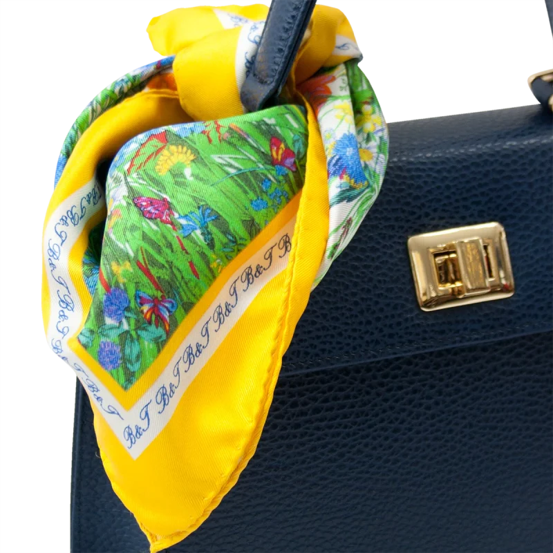 Foulard piccolo in seta gialla con fantasia floreale utilizzato su borsa blu in pelle